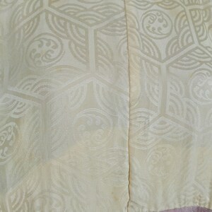 May include: A cream-colored kimono with a geometric pattern and a pink bottom half. The kimono is made of a silky fabric and has a traditional Japanese design.