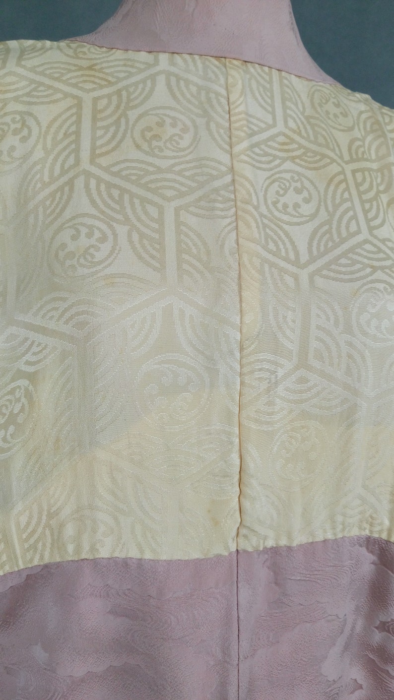 May include: A cream-colored kimono with a geometric pattern and a pink bottom half. The kimono is made of a silky fabric and has a traditional Japanese design.