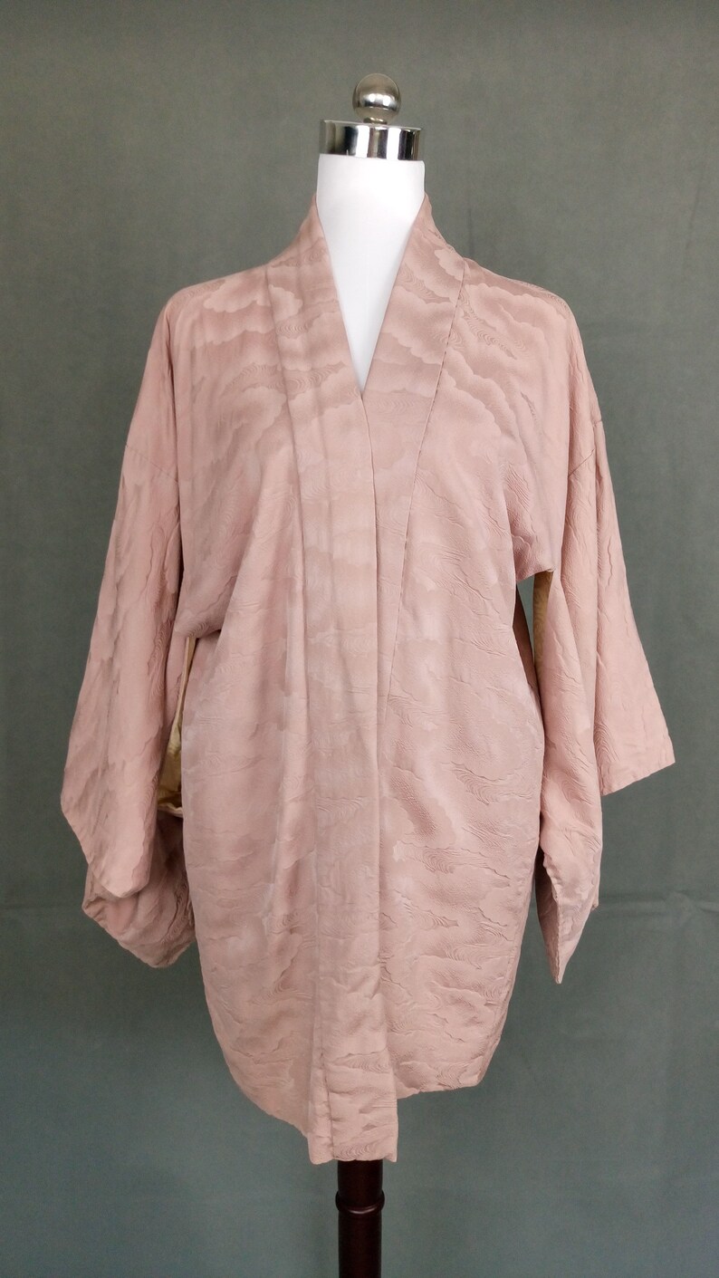 May include: A pale pink kimono with a subtle cloud pattern. The kimono is made of a soft, silky fabric and has a relaxed fit.