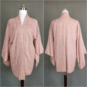 May include: A pale pink Japanese kimono with a subtle wave pattern. The kimono is made of a soft, silky fabric and has long sleeves.
