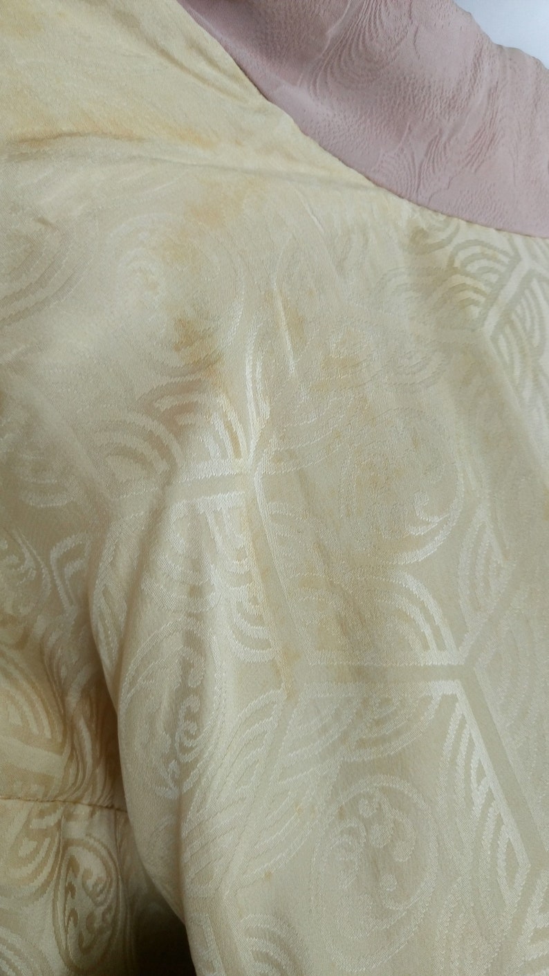 May include: Close-up of a cream-colored fabric with a subtle embossed pattern. The fabric has a few light brown stains.