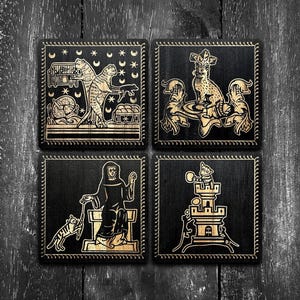 May include: A set of four square black wooden coasters featuring intricate gold-colored engravings. The designs depict medieval-style illustrations of cats in various scenes, including a cat in a tower, a cat with a person, and celestial motifs.