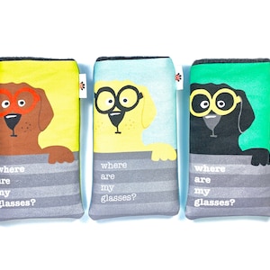 Puede incluir: Tres estuches de gafas coloridos con ilustraciones de perros con gafas. Los estuches son marrones, amarillos y negros, cada uno con un color de fondo diferente. El texto "where are my glasses?" está impreso en cada estuche.