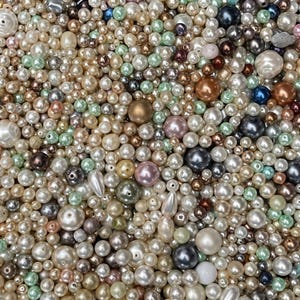 May include: A large collection of loose beads in various sizes and shapes, featuring a mix of colors including white, cream, soft pink, light green, bronze, brown, and dark gray. The beads have smooth, glossy, and metallic finishes.