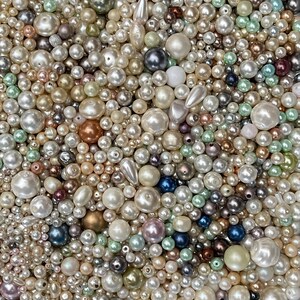 May include: A large collection of loose beads in various sizes and shapes, featuring a mix of white, cream, metallic gold, bronze, silver, soft pink, light blue, and mint green colors with smooth, lustrous, and pearlescent finishes.