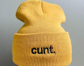 May include: A mustard yellow beanie with the word "cunt" embroidered in black.