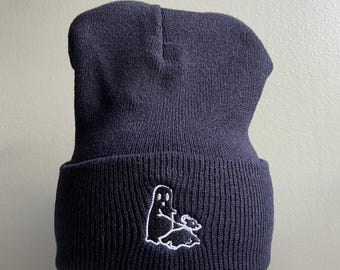 May include: Black beanie with a white embroidered ghost design. The ghost is sitting on a cloud with a small smile.