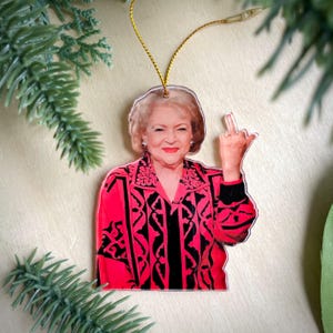May include: A red and black patterned Christmas ornament featuring a portrait of a woman with a mischievous expression, giving the middle finger.