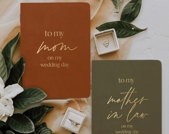 May include: Two brown and green journals with gold lettering. The top journal says "to my mom on my wedding day". The bottom journal says "to my mother in law on my wedding day".