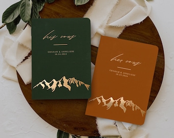 May include: Two green and orange leather-bound journals with gold foil lettering that reads "his vows" and "her vows". The journals have a mountain range design in gold foil.