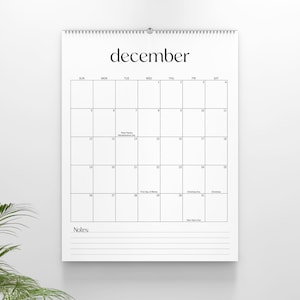 May include: A white wall calendar for the month of December with black text and grid lines. The calendar features a spiral binding at the top and a dedicated section for notes at the bottom with horizontal lines for writing.