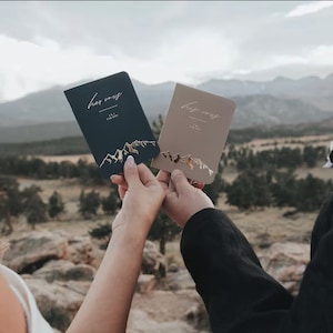 May include: Two small, hardcover journals with gold foil mountain illustrations and the words "her vows" and "his vows" on the covers.