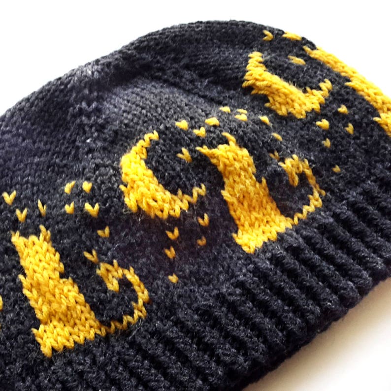 Op de afbeelding: Zwarte gebreide beanie met een geel gebreid "LOVE" ontwerp.