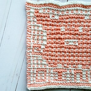 K&ouml;nnte beinhalten: Ein gestrickter Geschirrtuch mit einem Pfirsich- und Wei&szlig;muster. Das Geschirrtuch ist mit einem strukturierten Stich gefertigt.