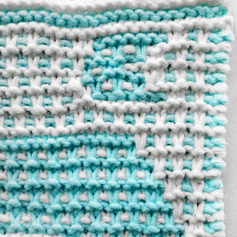 May include: Close-up of a knitted fabric with a white and light blue pattern. The fabric is made of yarn and has a textured surface.