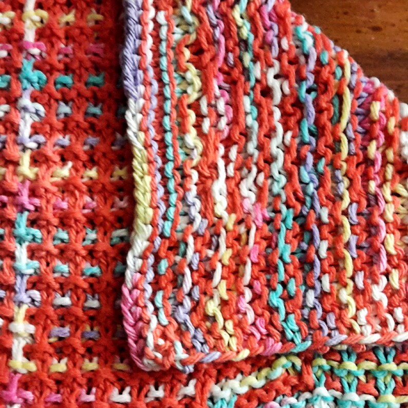 May include: A close-up of a knitted dishcloth with a colorful striped pattern in shades of orange, pink, white, yellow, and blue.