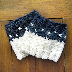 May include: A pair of knitted leg warmers with a white bottom and a dark blue top with white snowflake embroidery.