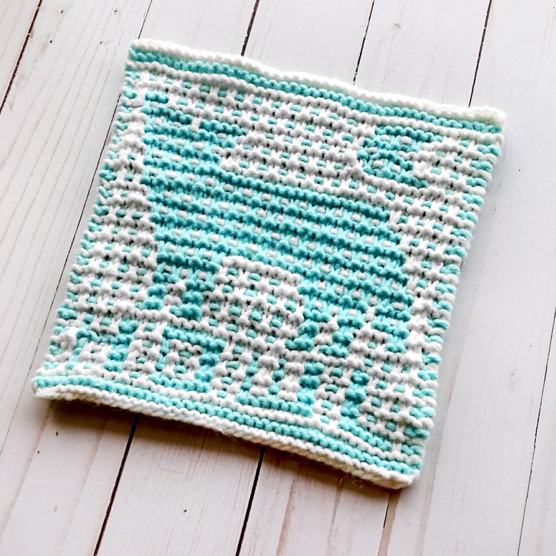 May include: A knitted dishcloth in a white and turquoise colour scheme. The dishcloth is made with a simple stitch pattern and has a square shape.