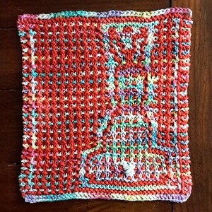 May include: A colorful knitted dishcloth with a geometric pattern in shades of red, white, blue, green, and purple.