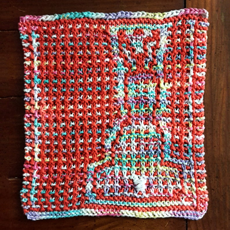 May include: A colorful knitted dishcloth with a geometric pattern in shades of red, white, blue, green, and purple.