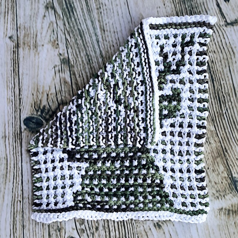 May include: A knitted dishcloth with a white border and a patchwork design of green, white, and brown squares.