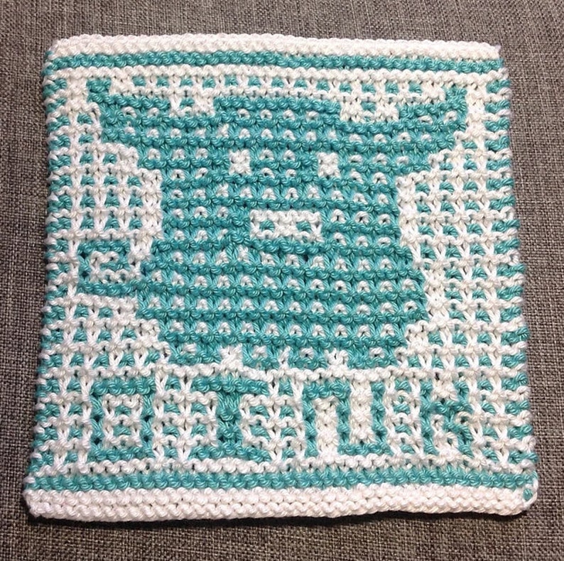 K&ouml;nnte beinhalten: Ein wei&szlig;er gestrickter Geschirrtuch mit einem blaugr&uuml;nen Design einer Teetasse und den Worten "tea time".