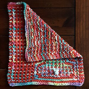 May include: A colorful knitted dishcloth with a red, white, and blue color scheme. The dishcloth is folded in half and has a textured pattern.