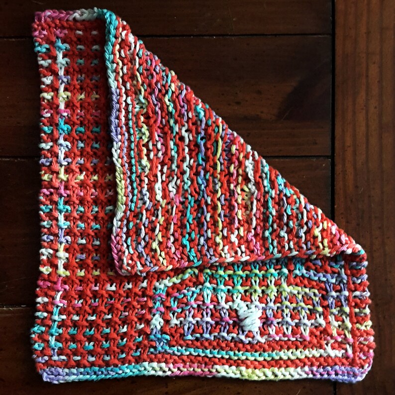 May include: A colorful knitted dishcloth with a red, white, and blue color scheme. The dishcloth is folded in half and has a textured pattern.