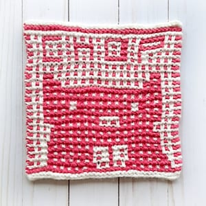 May include: A pink and white knitted dishcloth with a geometric pattern. The dishcloth is made with a textured yarn and has a square shape.