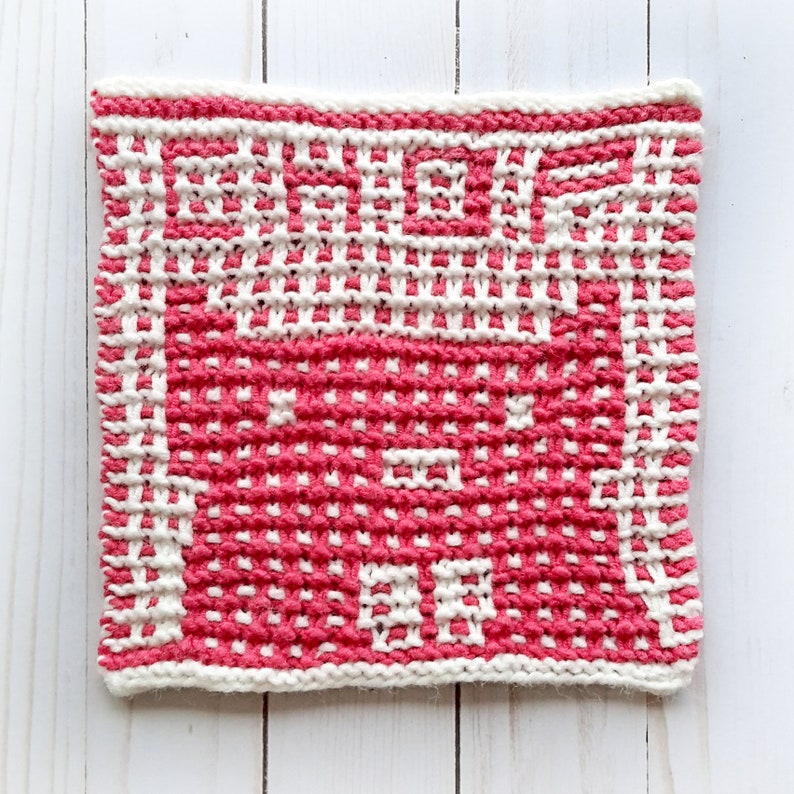 May include: A pink and white knitted dishcloth with a geometric pattern. The dishcloth is made with a textured yarn and has a square shape.