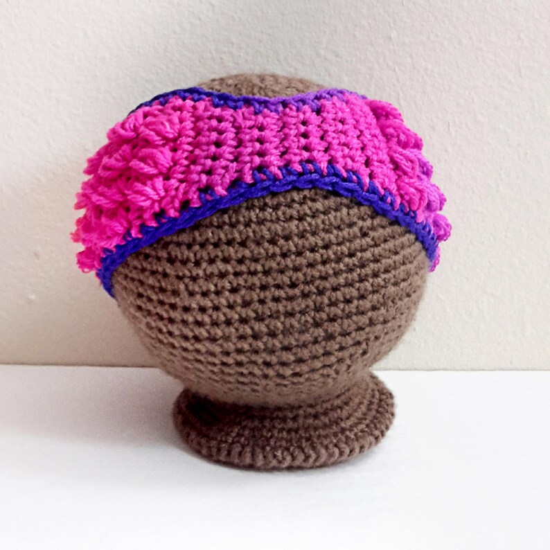 May include: A brown crocheted hat with a pink and purple crocheted band around the top.