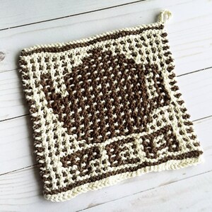 May include: A brown and white knitted pot holder with a square design. The pot holder has a loop for hanging.