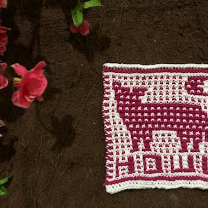 May include: A white and pink crocheted dishcloth with a geometric design of a stylised animal.