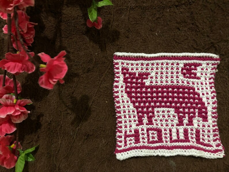 May include: A white and pink crocheted dishcloth with a geometric design of a stylised animal.