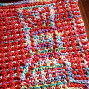 May include: Close-up of a knitted dishcloth with a colorful, multi-colored pattern. The dishcloth is made with a variety of yarn colors, including red, pink, white, blue, and yellow.