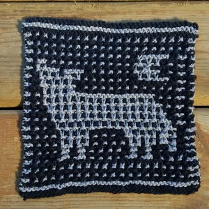 May include: A black and grey knitted square with a white design of a stylised animal, possibly a deer or a dog.
