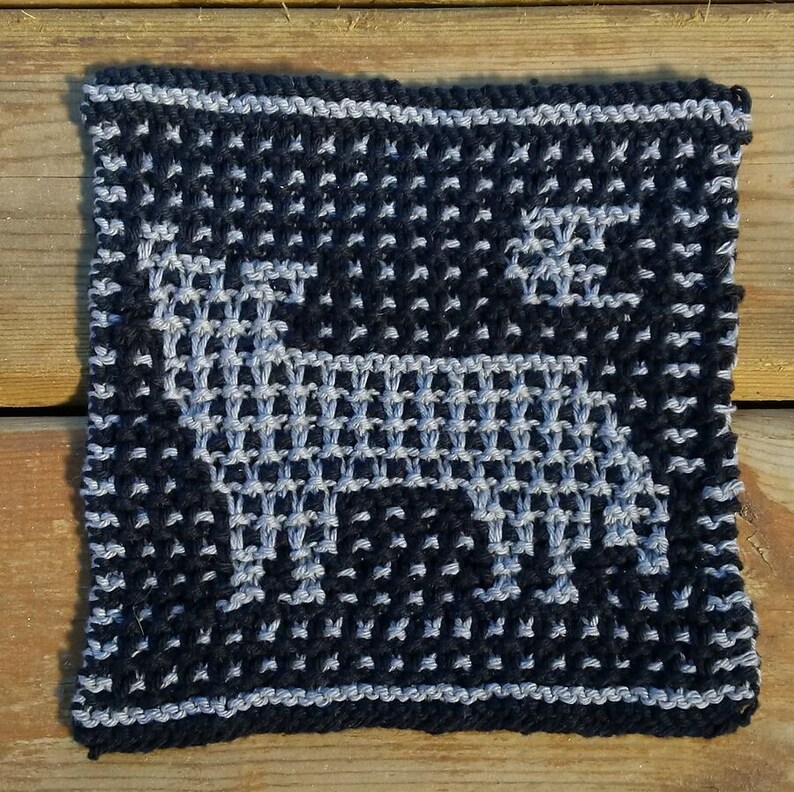 May include: A black and grey knitted square with a white design of a stylised animal, possibly a deer or a dog.