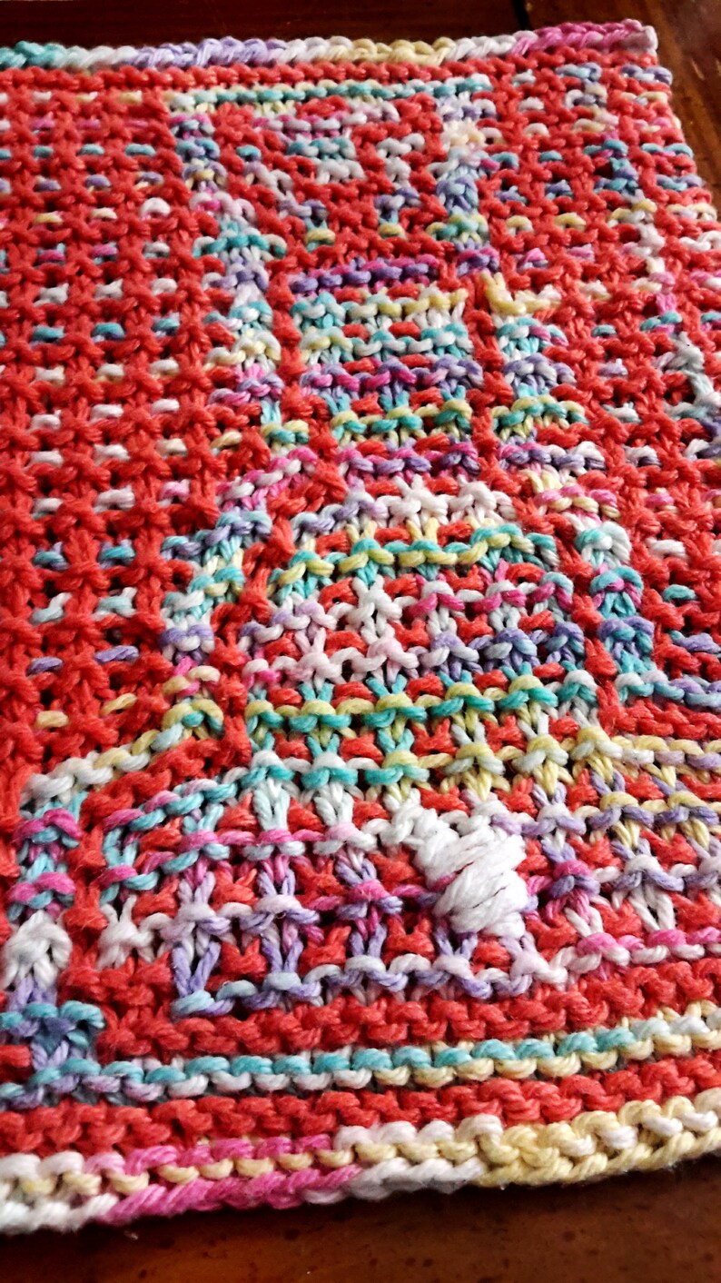 May include: A colorful knitted dishcloth with a variety of colors including red, pink, yellow, blue, and white.