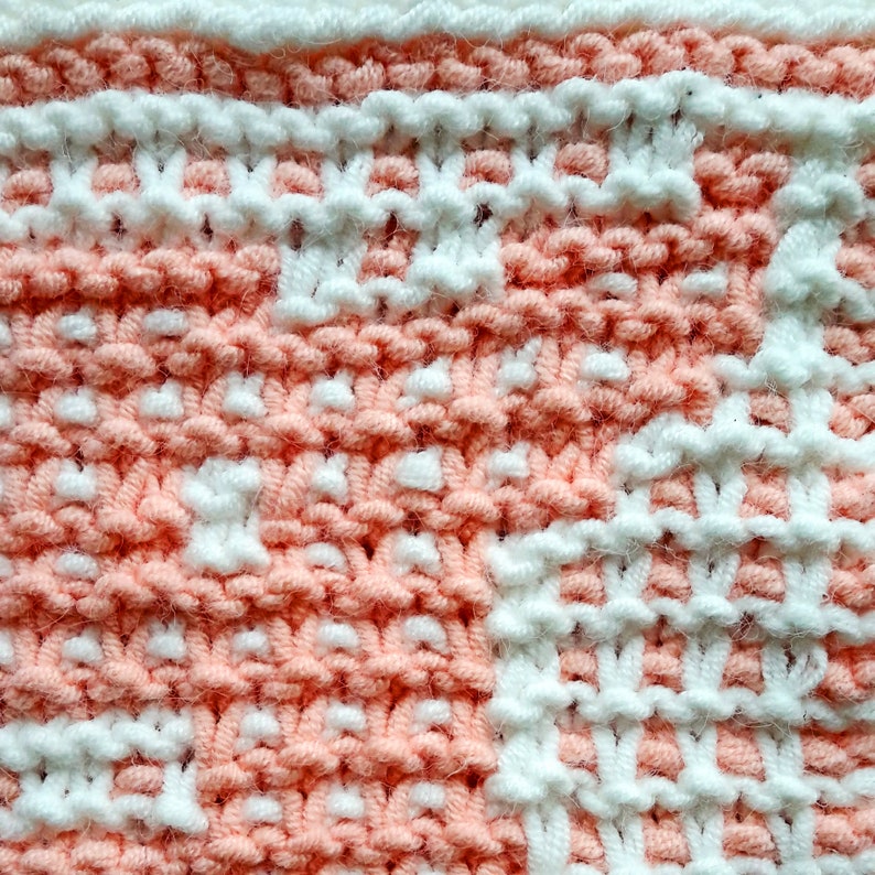 K&ouml;nnte beinhalten: Nahaufnahme eines gestrickten Stoffes mit einem rosa-wei&szlig;en Karomuster. Der Stoff ist aus weichem Garn gefertigt und hat eine strukturierte Oberfl&auml;che.