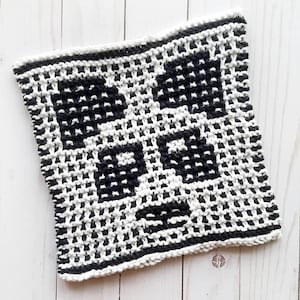 May include: Black and white knitted dishcloth with a geometric pattern. The dishcloth is made of cotton yarn and is approximately 7 inches square.