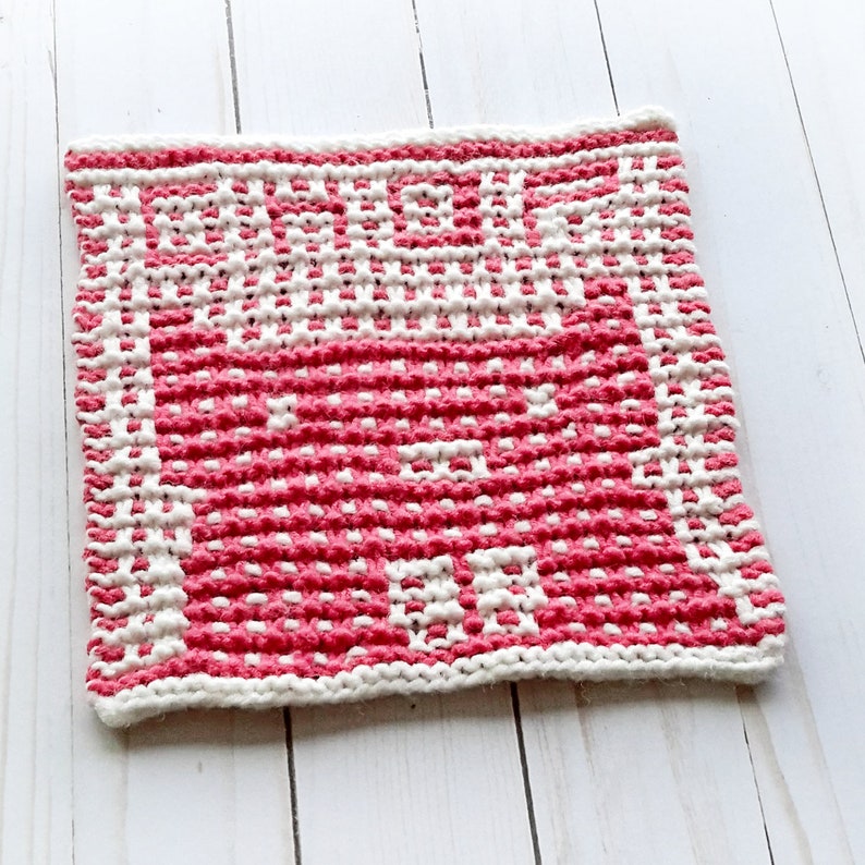 May include: A pink and white knitted dishcloth with a geometric pattern.