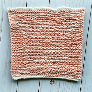 K&ouml;nnte beinhalten: Ein gestrickter Geschirrtuch in einem Pfirsich- und Wei&szlig;farbton. Das Geschirrtuch ist mit einer einfachen Strickmasche gearbeitet und hat eine leicht strukturierte Oberfl&auml;che.
