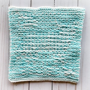 May include: A knitted dishcloth in a light blue and white colour scheme. The cloth is made with a simple knit stitch and has a slightly textured surface.