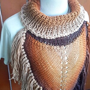 Pode incluir: Um xale triangular de malha com franjas em tons de marrom, laranja e bege. O xale &eacute; exibido em um manequim branco.