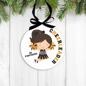 May include: White round ornament with a cartoon cheerleader holding pom-poms. The cheerleader is wearing a black and gold uniform with the word "CHARLOTTE" on it. The text "GO PANTHERS!" is on the ornament. The text "CHEERLEADER" is written around the edge of the ornament.
