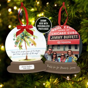 May include: A pair of round Christmas ornaments with a watercolor palm tree and a photo of a family in front of a Wrigley Field sign. The ornament on the left has the text "Gone of it's magic, some of it's tragic, but I had a good life all the way." and "Jimmy Buffett 1946-2023". The ornament on the right has the text "Thanks for the Memories, Jimmy".