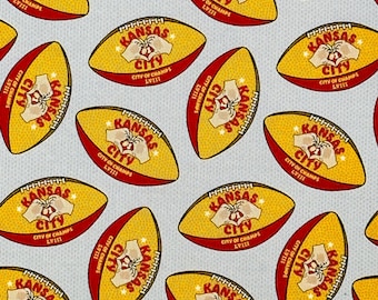May include: A repeating pattern of yellow and red footballs with the words "Kansas City" and "City of Champs" on them. The footballs are on a white background with a subtle texture.