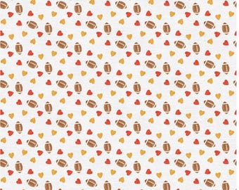 May include: White fabric with a repeating pattern of brown footballs, red hearts, and yellow hearts. The footballs are oval-shaped with brown stripes, and the hearts are in a simple, solid design.
