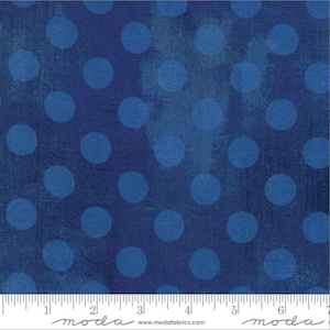 May include: A fabric with a dark blue background and large, lighter blue polka dots. The fabric has a textured appearance, with a subtle, distressed effect. The bottom of the image shows a ruler with the word "moda" printed on it.