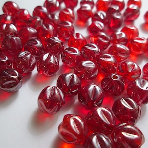 May include: A collection of red glass beads with a faceted design. The beads are scattered on a white surface.